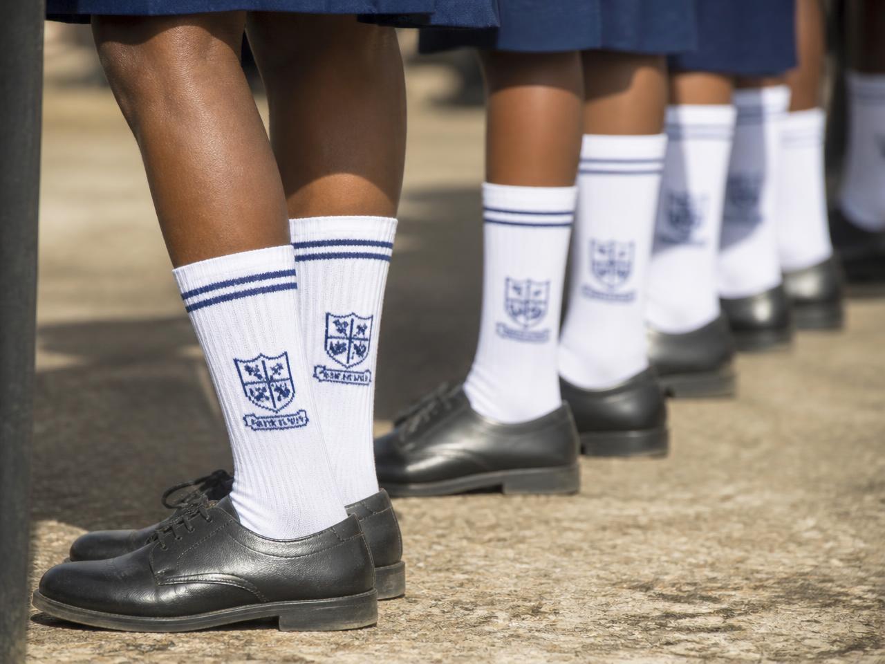 Row of pupils' legs in black school shoes and white crested knee-high school socks at assembly